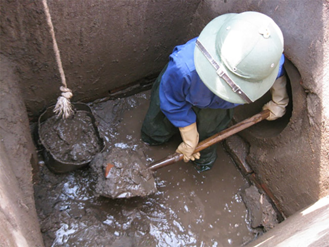 Dọn lớp bùn đáy ở hầm tự hoại (hầm cầu) bằng thủ công.